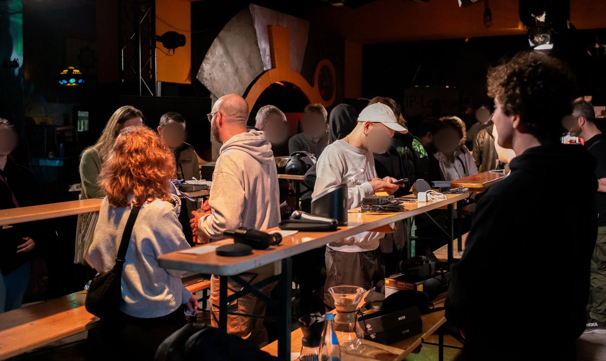 A large group of people standing between tables covered in electronics